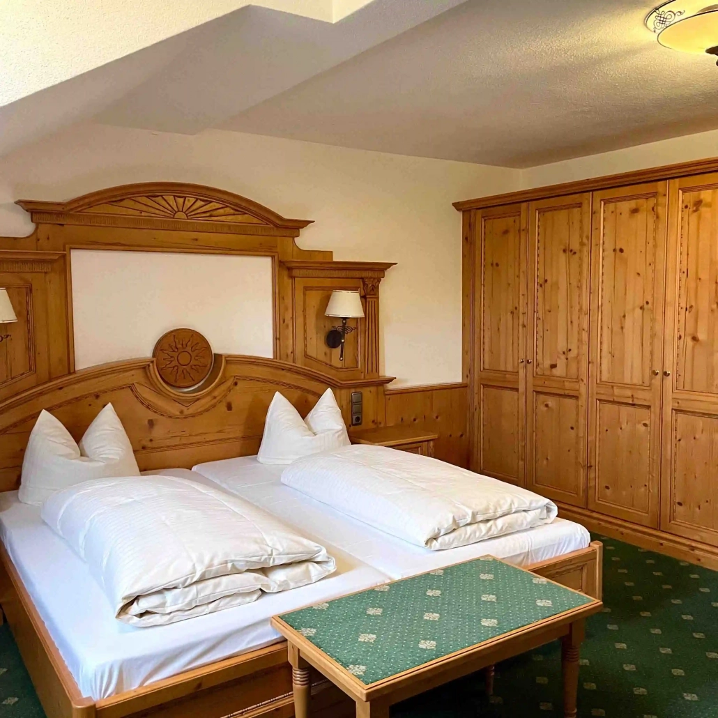 Doppelbettzimmer mit Holzmöbeln und weißer Bettwäsche auf grün gemustertem Teppichboden